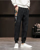 Black corduroy joggers with a printed side panel and ribbed cuffs, worn with a white sweatshirt and white sneakers