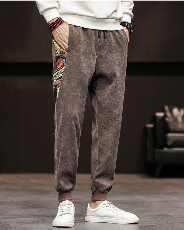 Brown corduroy joggers with a printed side panel and ribbed cuffs, worn with a white sweatshirt and white sneakers