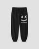 Black cotton jogger pants with a white crossed-out-eyes smiley print on the thigh, laid flat