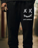 Black jogger pants with a white smiley print on the thigh, worn standing, front view