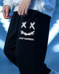 Black jogger pants with a white smiley print, side view on a blue background