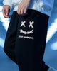 Black jogger pants with a white smiley print, side view on a blue background