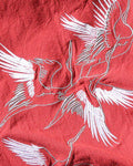 Close-up of the white-and-silver embroidered cranes on the red cotton-linen fabric