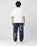 Model seen from behind in the navy crane-embroidered jogger pants, a white tee and white sneakers