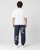 Model seen from behind in the navy crane-embroidered jogger pants, a white tee and white sneakers