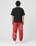 Model seen from behind in the red crane-embroidered jogger pants, a black tee and white sneakers