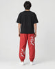 Model seen from behind in the red crane-embroidered jogger pants, a black tee and white sneakers