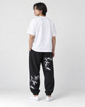 Model seen from behind at an angle in the black crane-embroidered jogger pants, a white tee and white sneakers