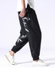 Black crane-embroidered jogger pants in motion, with the white cranes and the elastic cuff in view