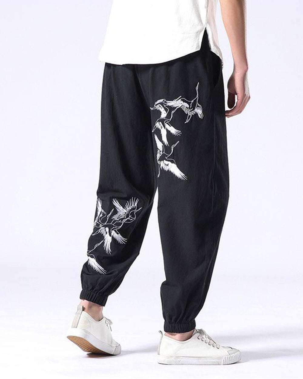 Black crane-embroidered jogger pants seen from behind, with white cranes on the right thigh and around the left calf