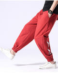 Red crane-embroidered jogger pants in motion, seen from the side with the elastic cuff above white sneakers