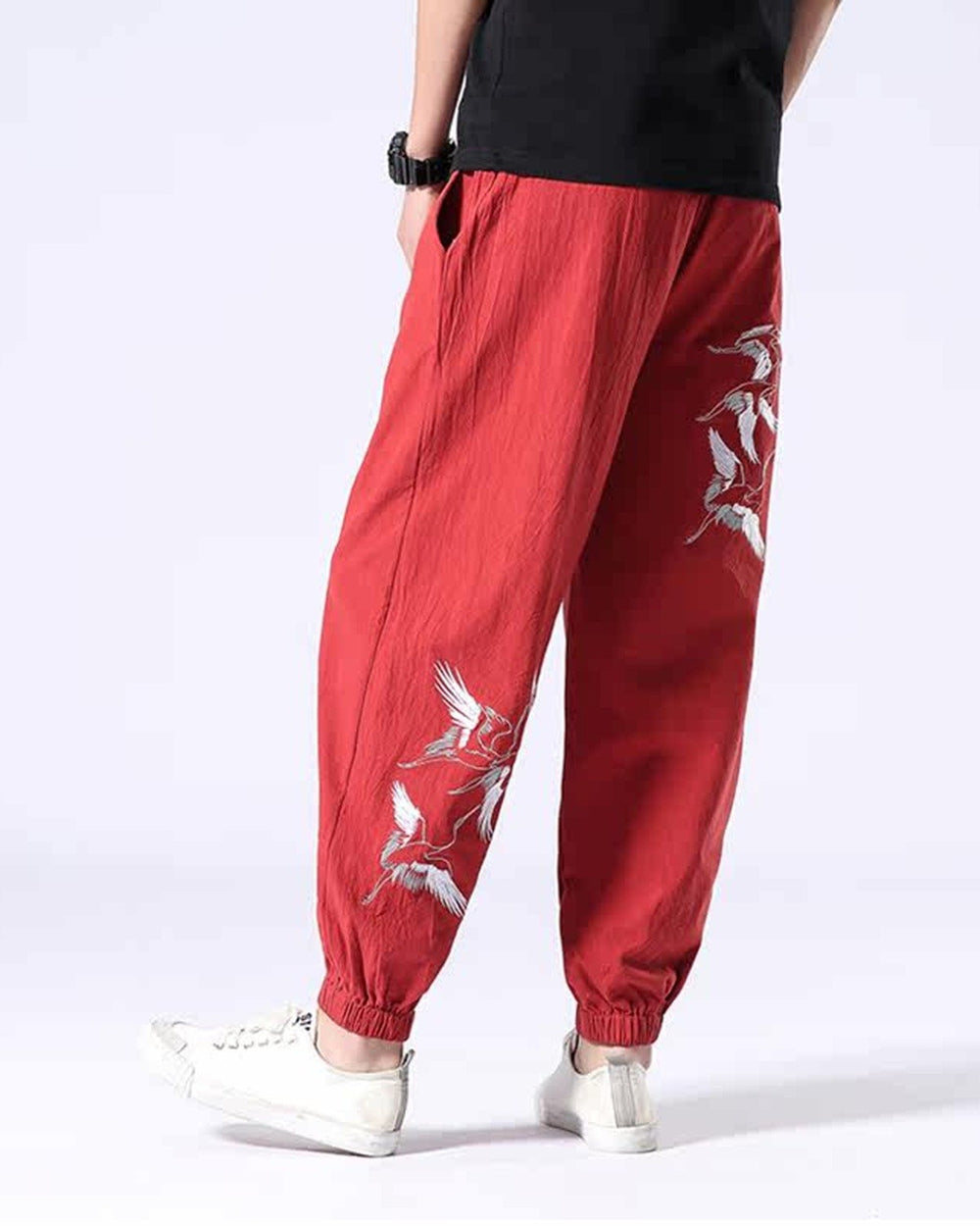 Red crane-embroidered jogger pants seen from behind, with cranes down the right thigh and around the left calf