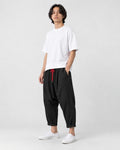 Model wearing the black crinkled harem pants with a white tee and white sneakers, three-quarter view