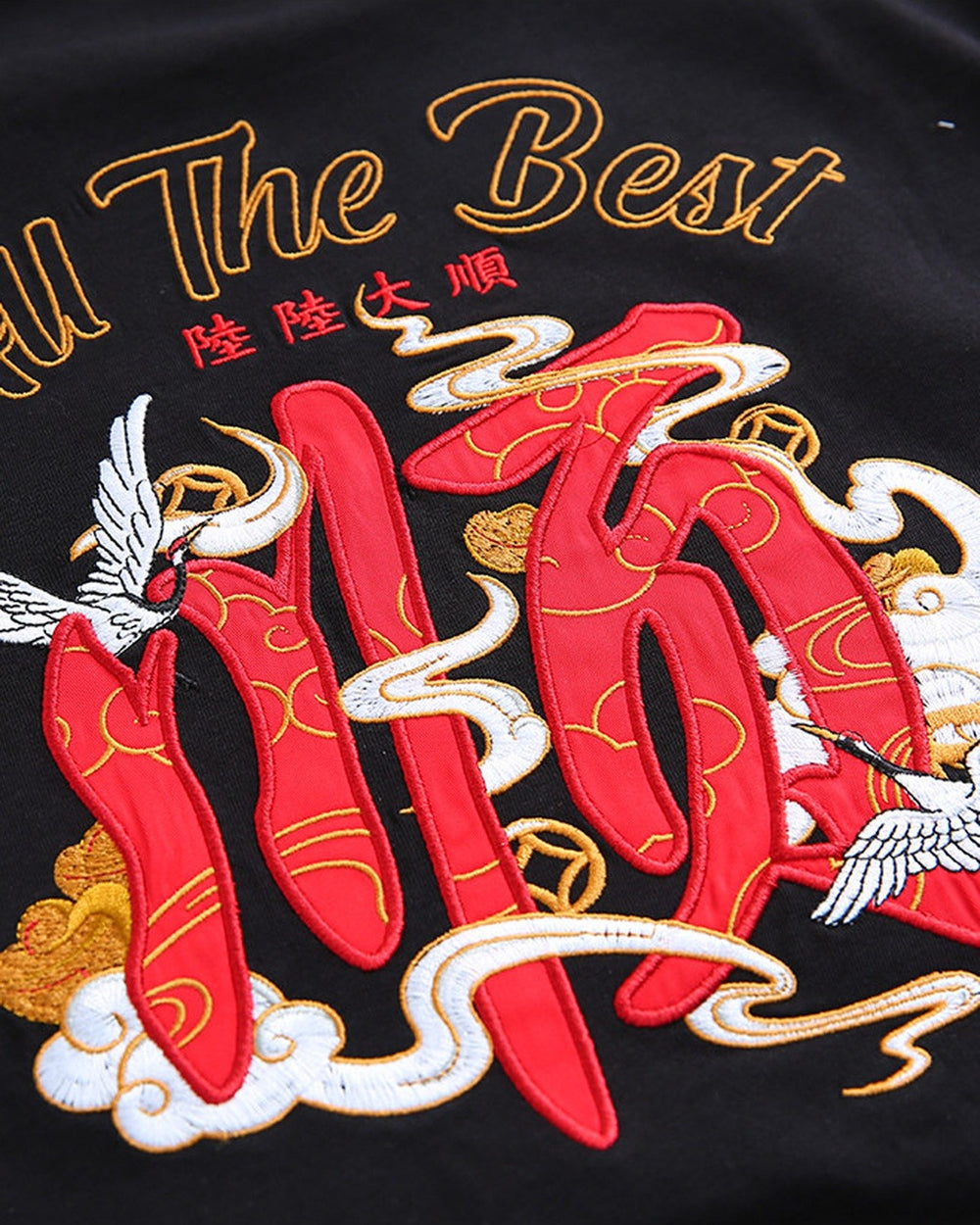 Close-up of the red character, cranes and gold-thread script embroidered on the back of the black T-shirt