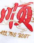 Close-up of the small red character and gold ALL THE BEST lettering embroidered on the chest of the white T-shirt