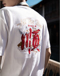 Man seen from behind in the white T-shirt, showing the red and gold embroidery across the upper back