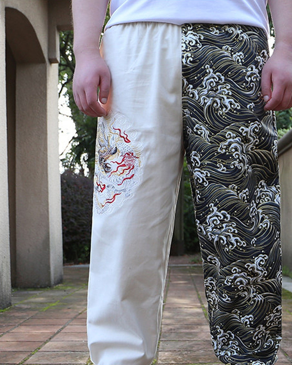 Man wearing the cream and wave-print jogger pants, with the embroidered dragon on the thigh and gathered cuffs