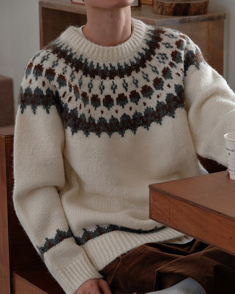 Man leaning on a table in the cream fair-isle sweater, showing the banded cuff and hem
