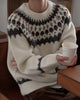 Man seated at a table in the cream fair-isle sweater, holding a paper cup