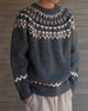 Charcoal gray fair-isle sweater with hands in the pockets, showing the zigzag hem band