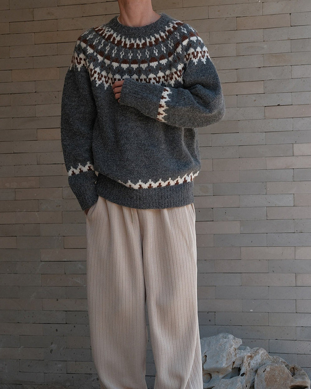 Man standing in a charcoal gray fair-isle yoke sweater with cream zigzag bands and beige trousers