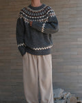 Man standing in a charcoal gray fair-isle yoke sweater with cream zigzag bands and beige trousers