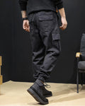 Black cargo joggers in motion, showing the flap pocket on the thigh and the elastic ankle cuff
