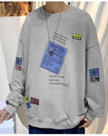 Light gray crewneck sweatshirt with a tilted blue label, a yellow tag and barcode patches on the sleeves