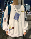 White crewneck sweatshirt with a blue label print, worn with a chain necklace on a city street
