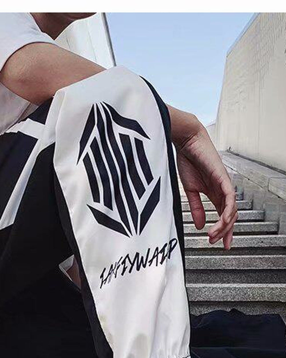 Close view of the hexagon emblem and script lettering on the white lower leg of the black joggers