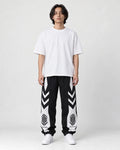 Man in black joggers with white chevron panels on the thighs and white lower legs, white tee and sneakers, full length