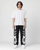 Man in black joggers with white chevron panels on the thighs and white lower legs, white tee and sneakers, full length
