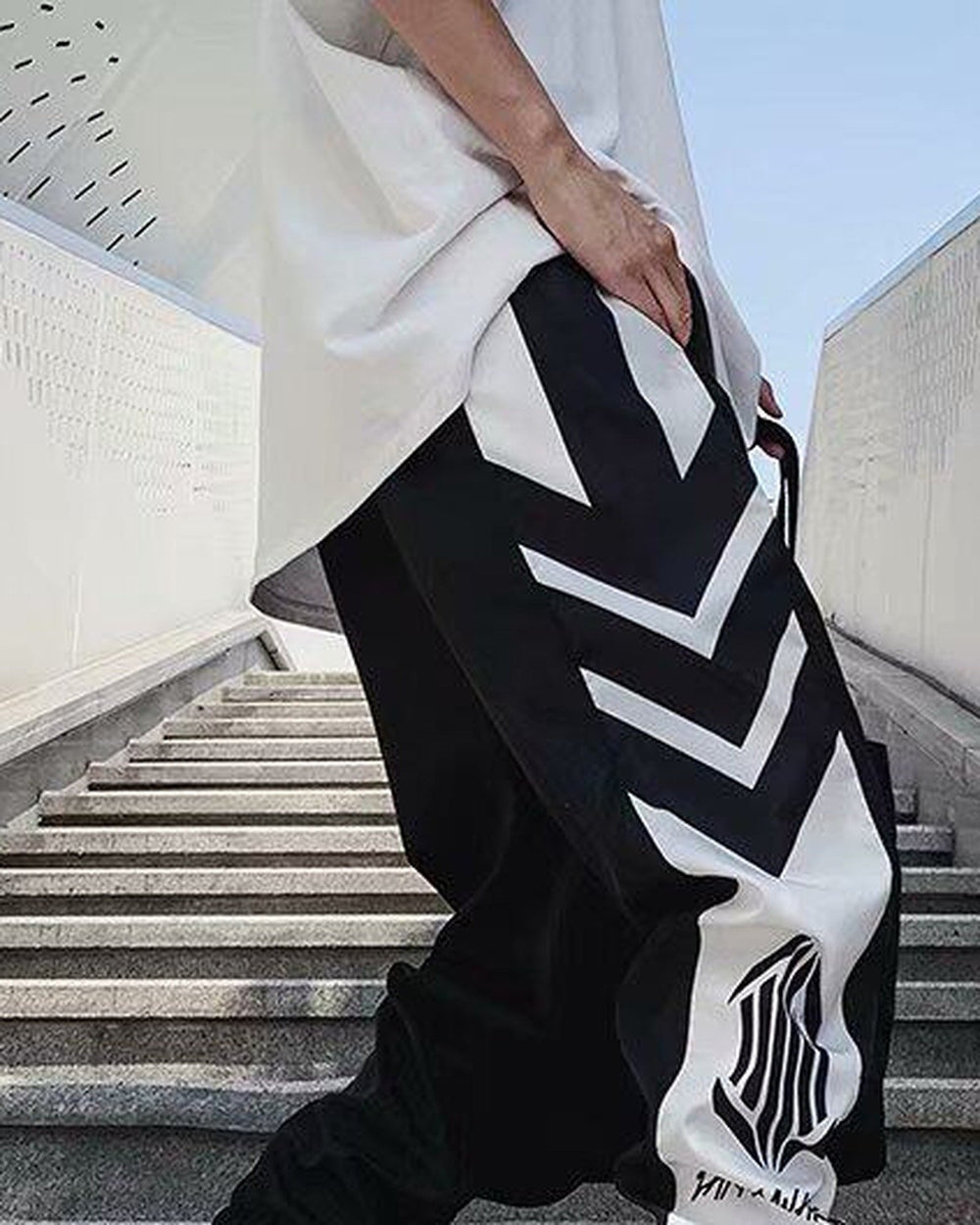 Black joggers with white arrow-shaped chevron panels down the thigh and a white lower leg with an emblem