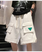 White knee-length cargo-pocket shorts with a green triangle patch, worn with a black tee, front view