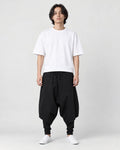 Model wearing the black layered drop-crotch harem pants with a white tee and white sneakers, front view