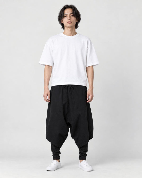 Model wearing the black layered drop-crotch harem pants with a white tee and white sneakers, front view