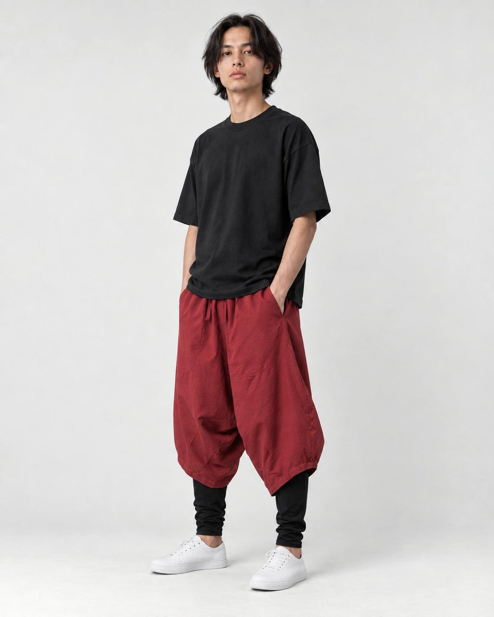 Model wearing the wine red layered drop-crotch harem pants with a black tee and white sneakers, three-quarter view