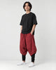 Model wearing the wine red layered drop-crotch harem pants with a black tee and white sneakers, three-quarter view