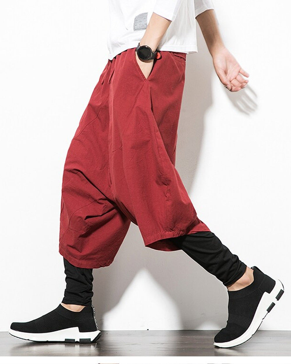 Wine red layered drop-crotch harem pants with a fitted black inner layer, worn with a white tee and black sock sneakers