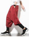 Wine red layered drop-crotch harem pants with a fitted black inner layer, worn with a white tee and black sock sneakers