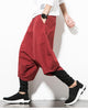 Wine red layered drop-crotch harem pants with a fitted black inner layer, worn with a white tee and black sock sneakers