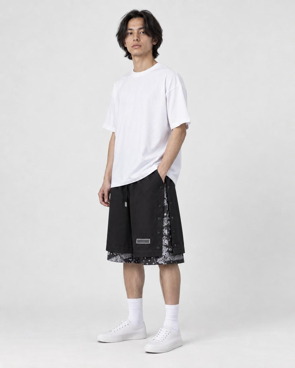 Model wearing the black layered paisley snap-side shorts with a white tee and white sneakers, three-quarter view