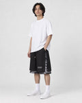 Model wearing the black layered paisley snap-side shorts with a white tee and white sneakers, three-quarter view