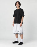 Model wearing the white layered paisley snap-side shorts with a black tee and black sneakers, three-quarter view