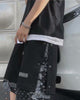 Black snap-side shorts from the side, with the snaps open along the seam and paisley cloth showing through