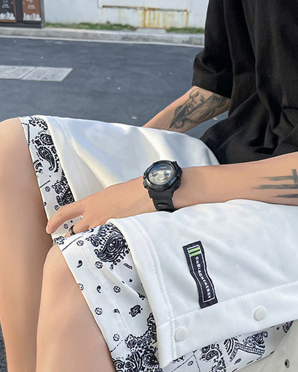 Seated man in the white snap-side shorts, showing the woven label, metal snaps and paisley layer at the hem