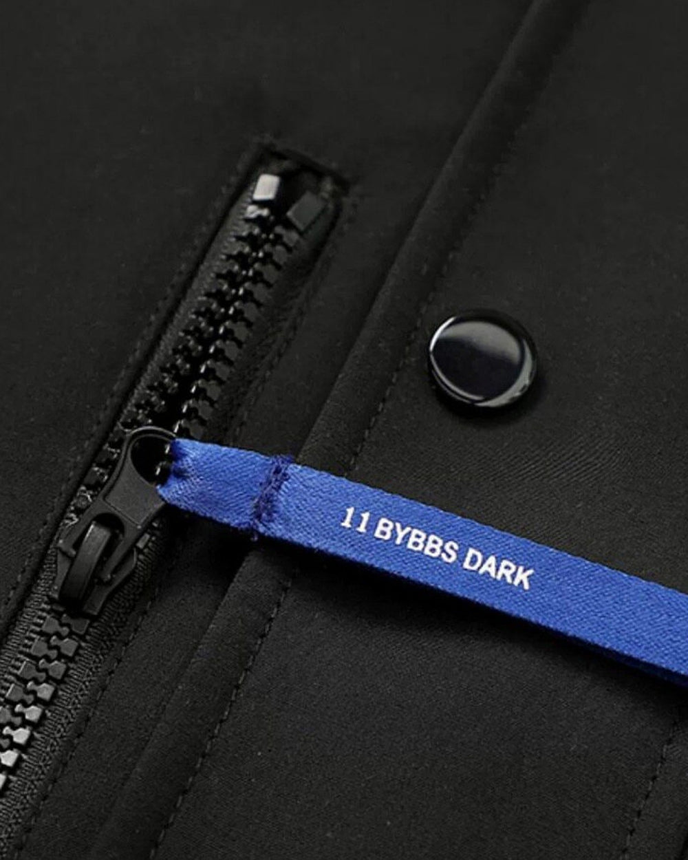 Close view of the blue ribbon zip pull and the snap button on the black jacket placket