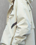 Side view of the beige hooded jacket showing the sleeve pocket and the hem