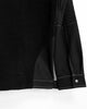 Close view of the curved smooth hem panel, snap strap and gray stitching on the black sweatshirt