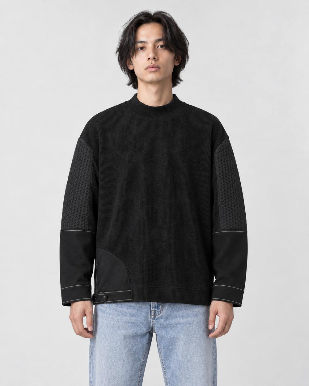 Man in a loose black mock-neck sweatshirt with quilted upper sleeves and light-wash jeans, torso to mid-thigh